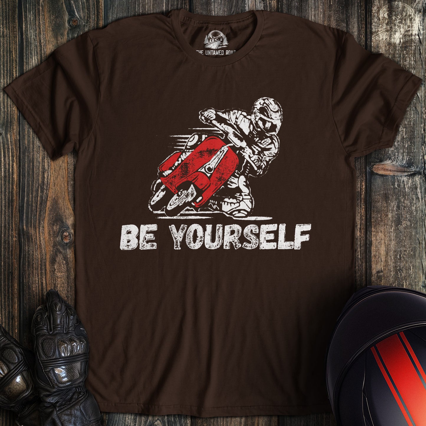A dark chocolate colored t-shirt with the words "be yourself" printed on the front.