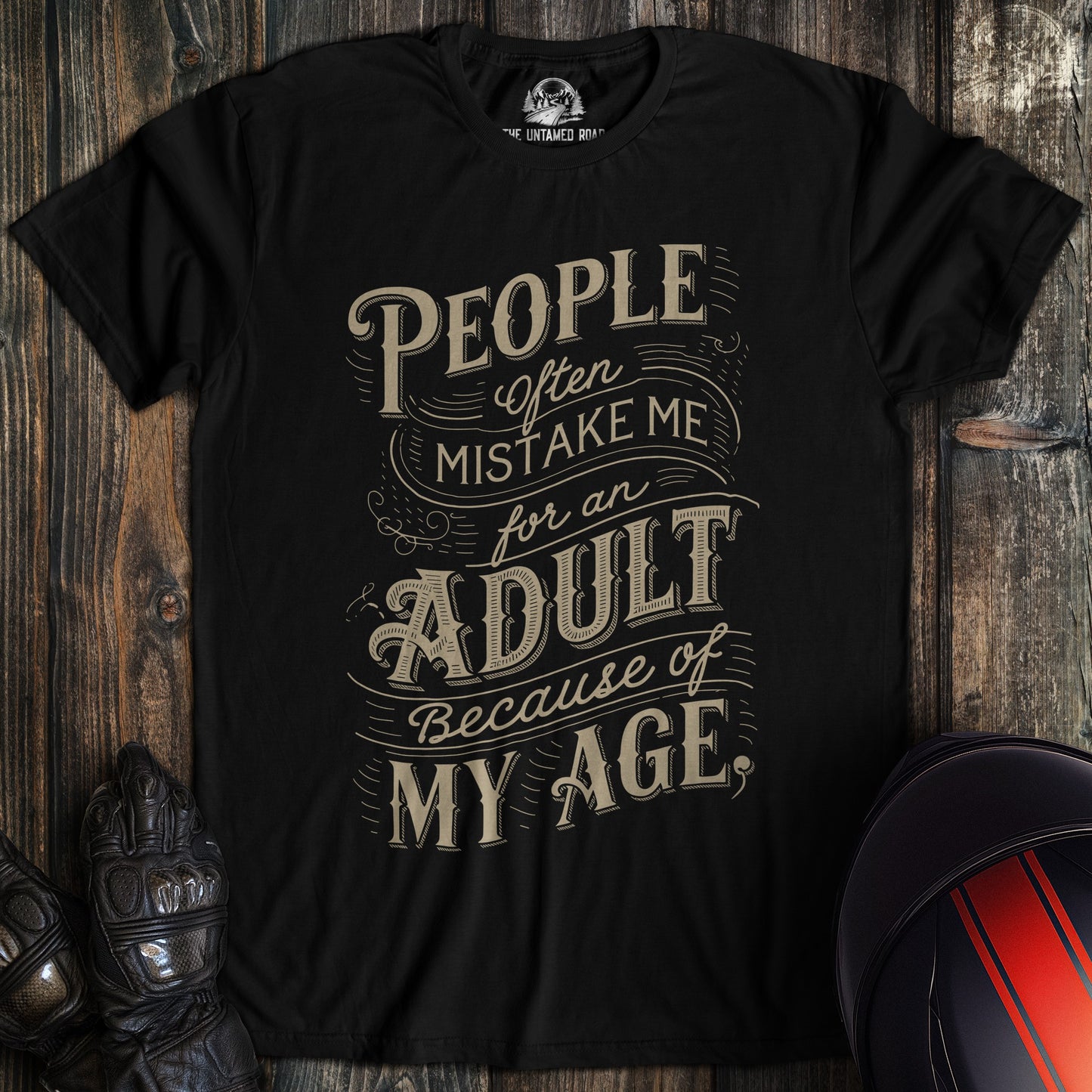 A black colored t-shirt with the words "mistake me for adult" printed on the front.