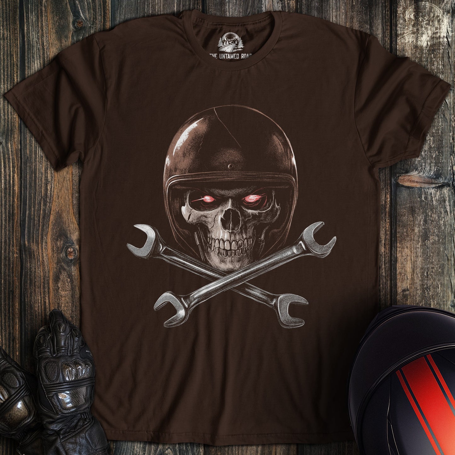 A dark chocolate colored t-shirt with the words "skull and wrenches" printed on the front.
