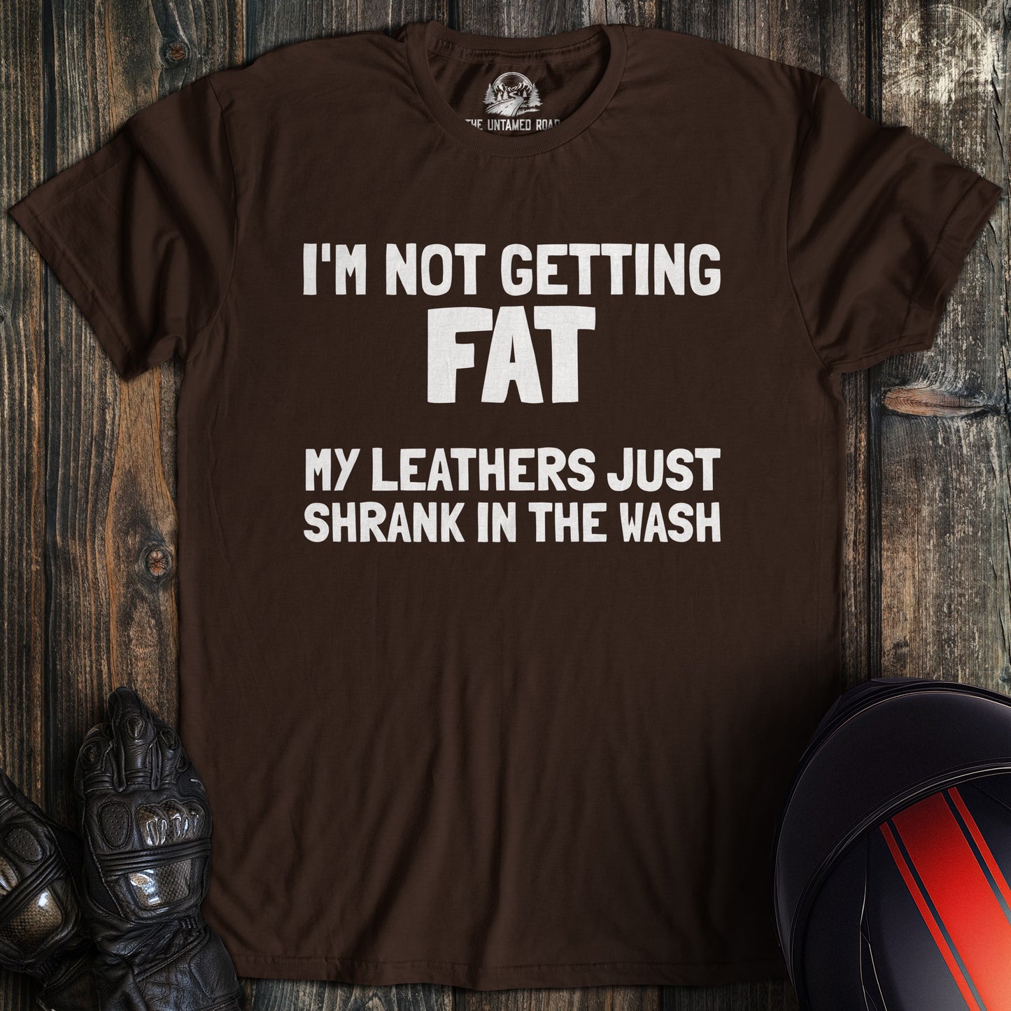 A dark chocolate colored t-shirt with the words "not fat leathers shrank" printed on the front.