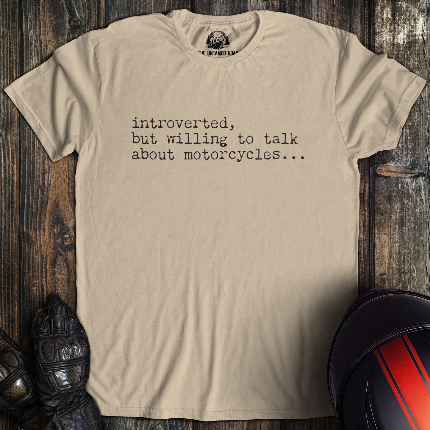 A sand colored t-shirt with the words "introverted but willing to talk" printed on the front.