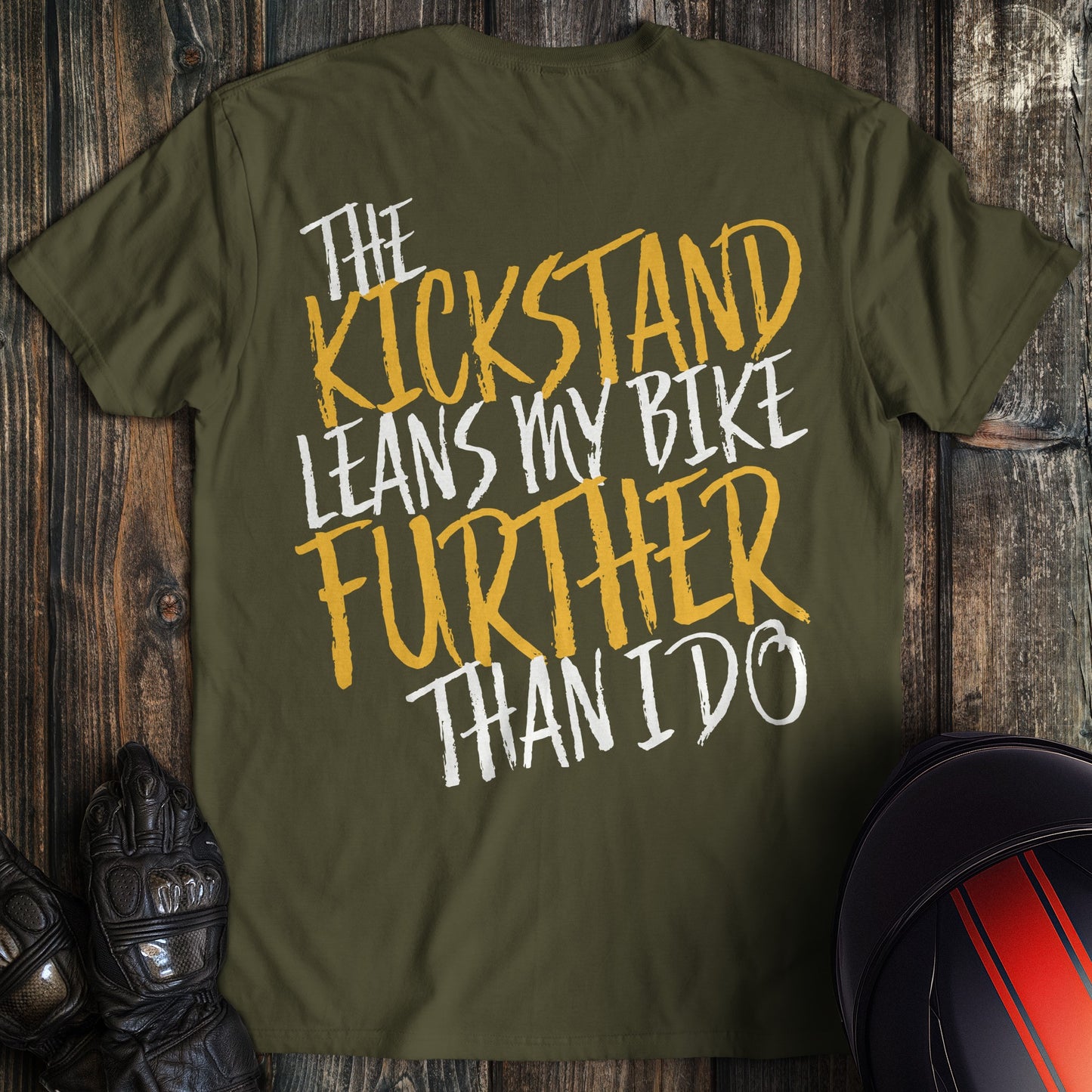 A military green colored t-shirt with the words "kickstand leans further" printed on the back.