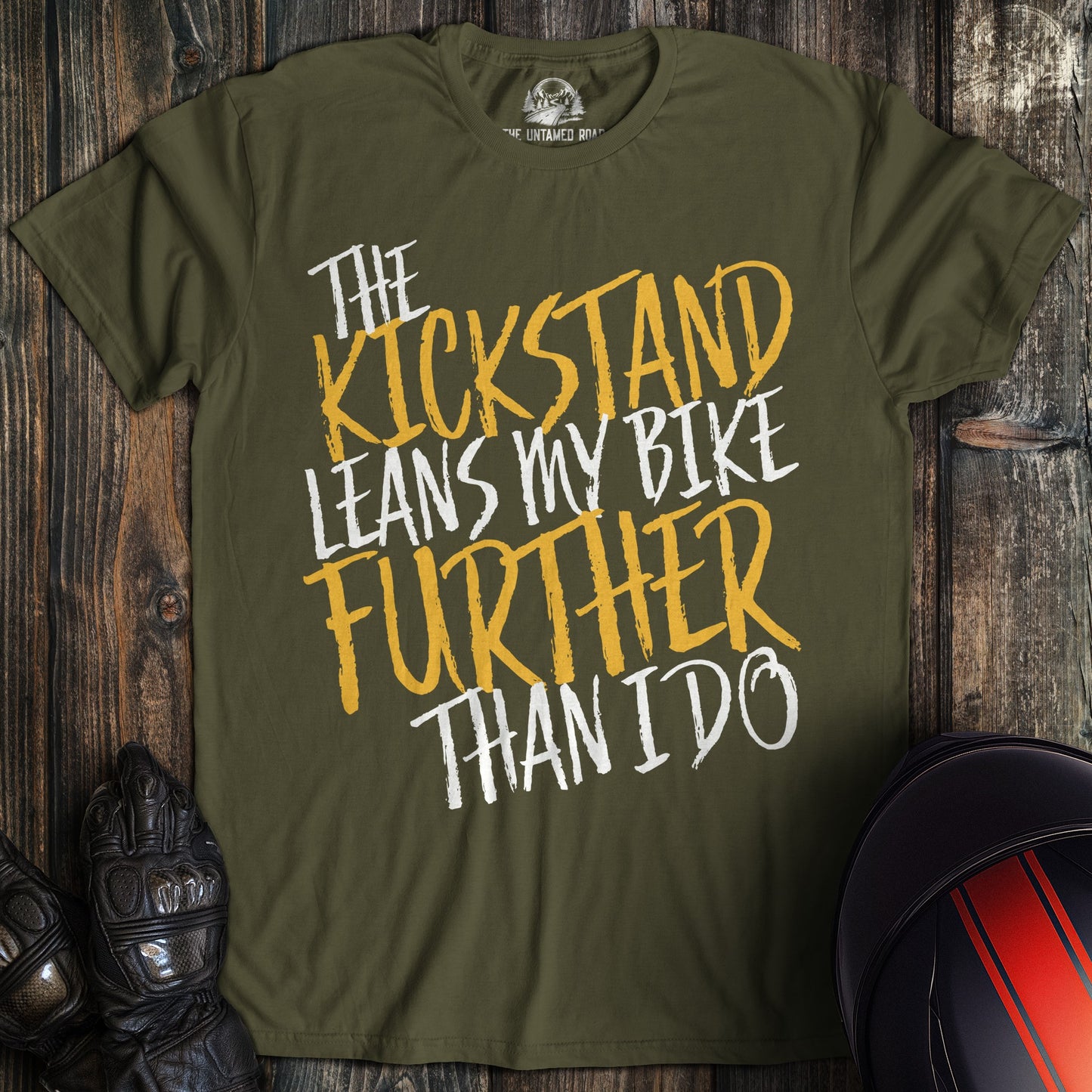 A military green colored t-shirt with the words "kickstand leans further" printed on the front.