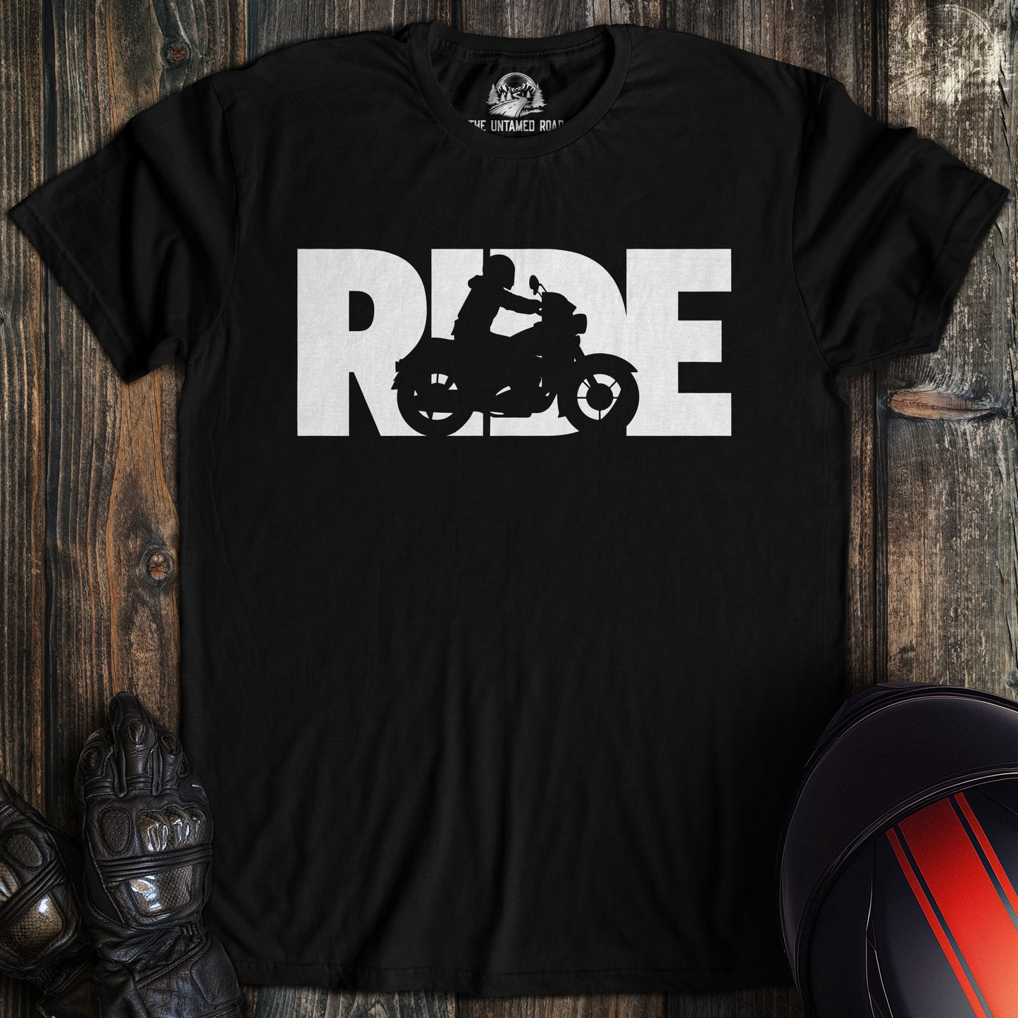 Black t-shirt with 'RIDE' graphic on a wooden surface with motorcycle helmet and glove.