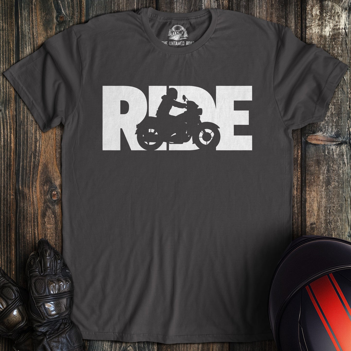 Black t-shirt with 'RIDE' graphic on a wooden surface with motorcycle gear.