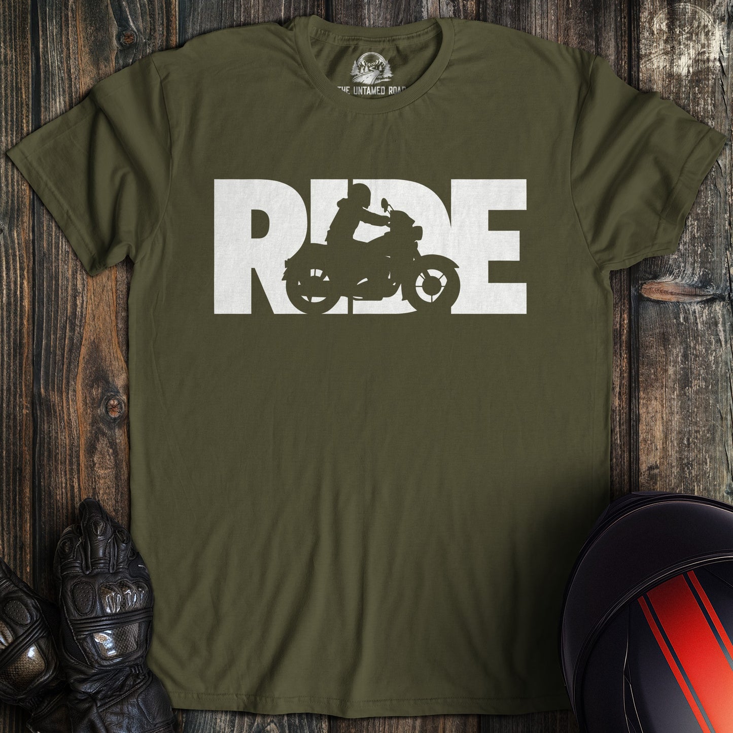 Green t-shirt with 'RIDE' graphic on a wooden surface with motorcycle gear.