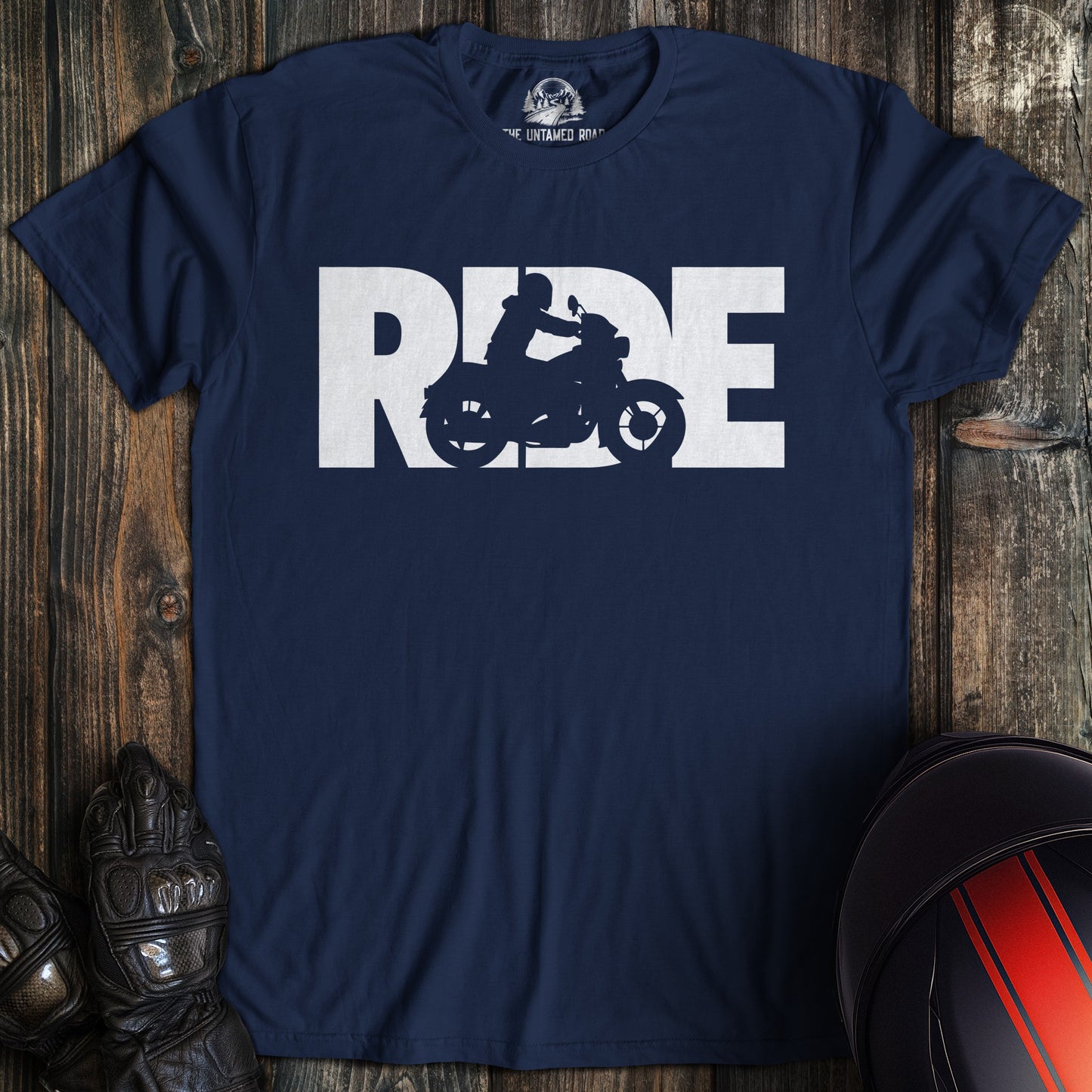Navy blue t-shirt with 'RIDE' graphic on a wooden surface with motorcycle helmet and gloves.