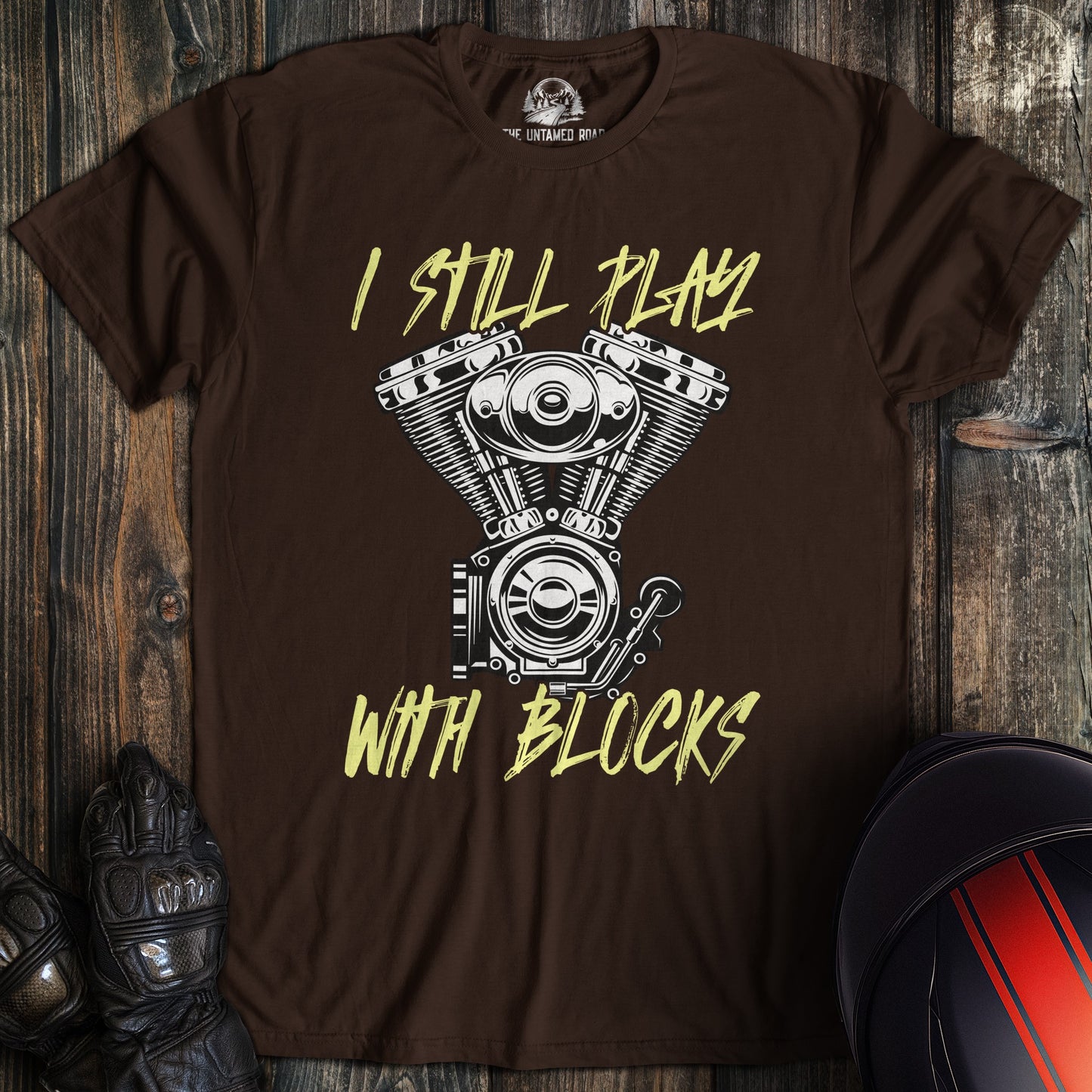 A dark chocolate colored t-shirt with the words "still play with blocks" printed on the front.