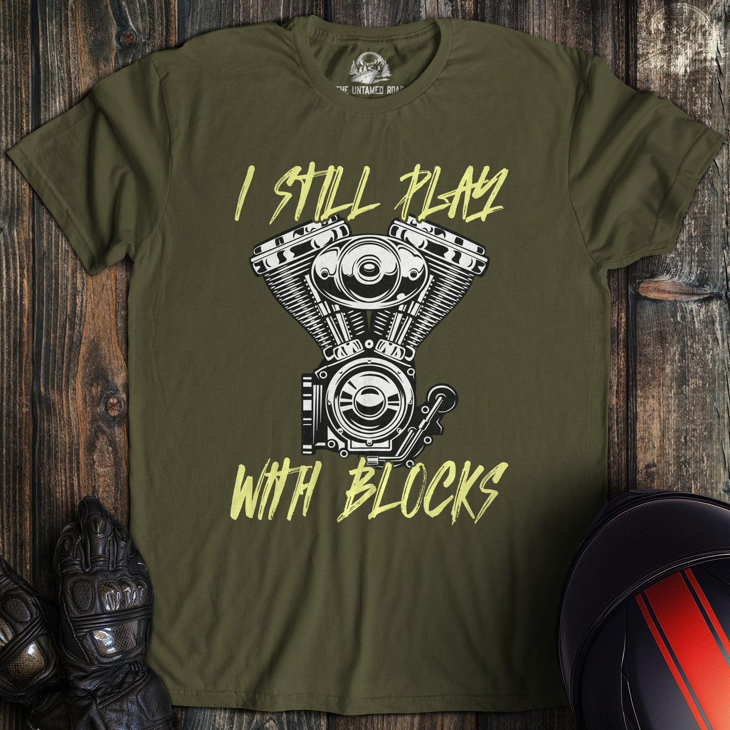 A military green colored t-shirt with the words "still play with blocks" printed on the front.