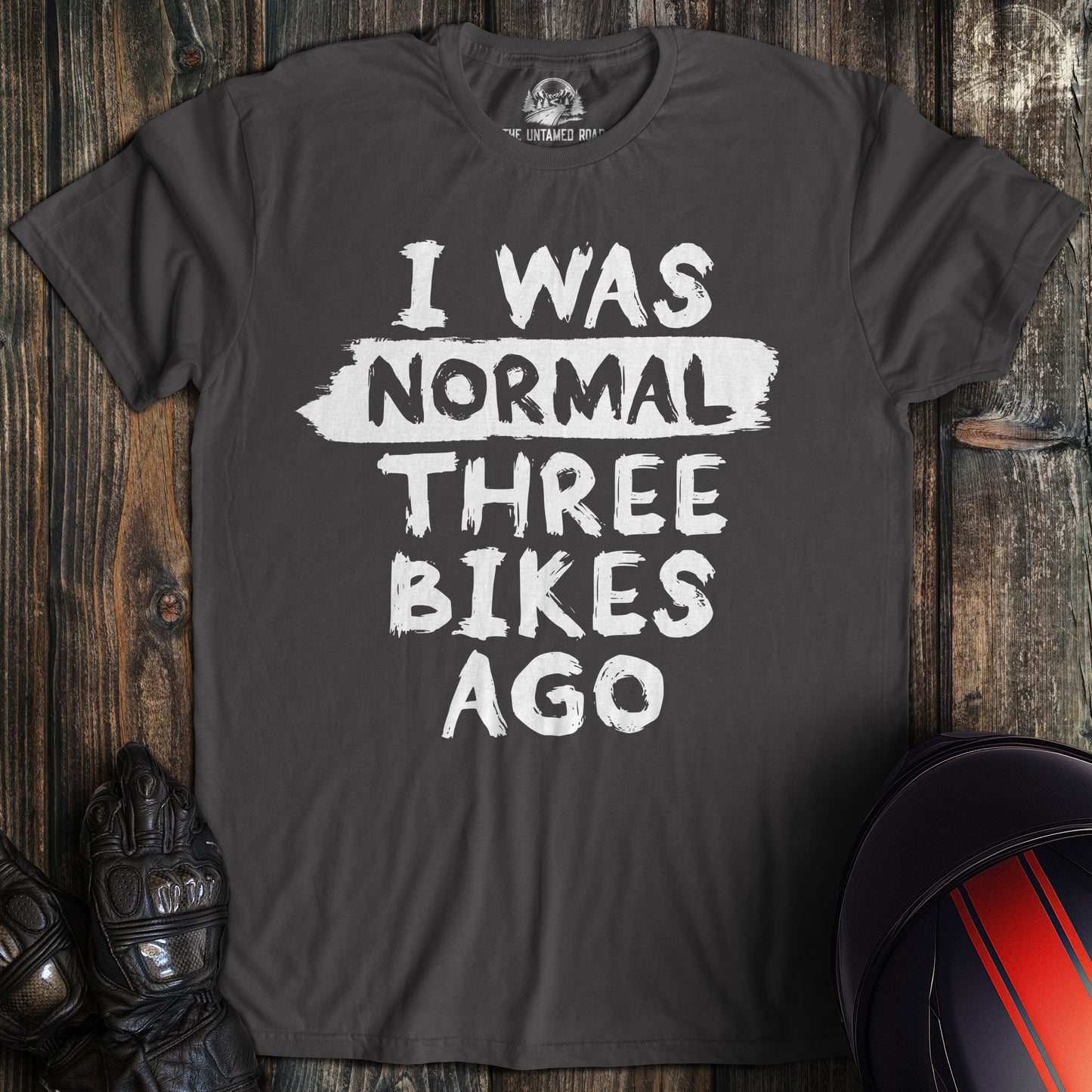 A charcoal colored t-shirt with the words "normal three bikes ago" printed on the front.