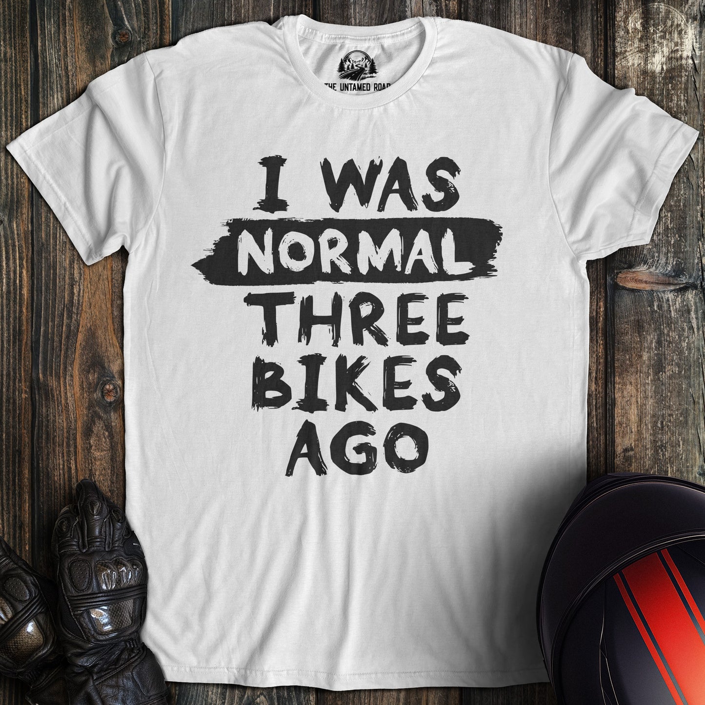 A white colored t-shirt with the words "normal three bikes ago" printed on the front.
