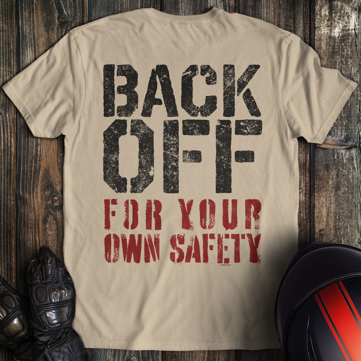 A sand colored t-shirt with the words "back off for your safety" printed on the back.