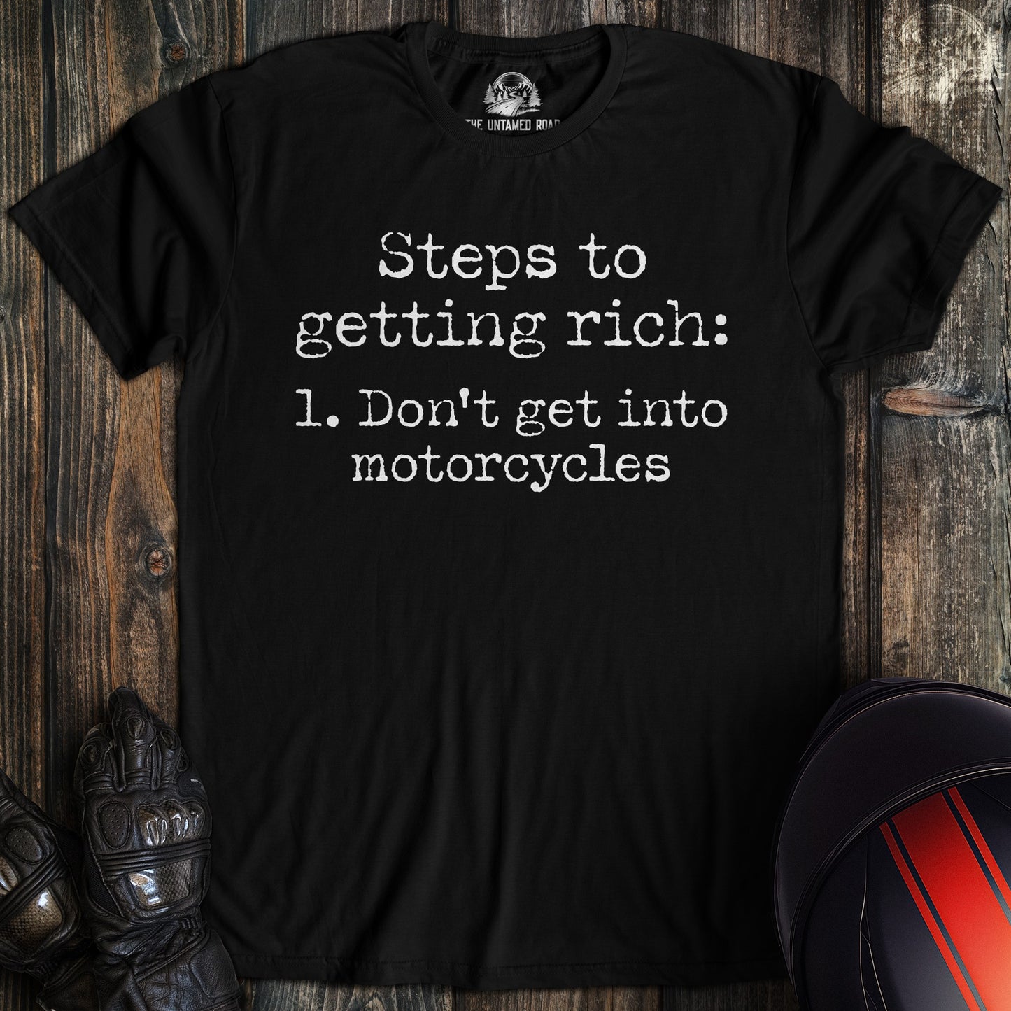 A black t-shirt with white text that reads, Steps to getting rich: 1. Don't get into motorcycles.