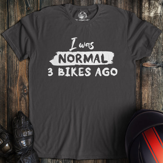 A charcoal colored t-shirt with the words "normal three bikes ago" printed on the front.