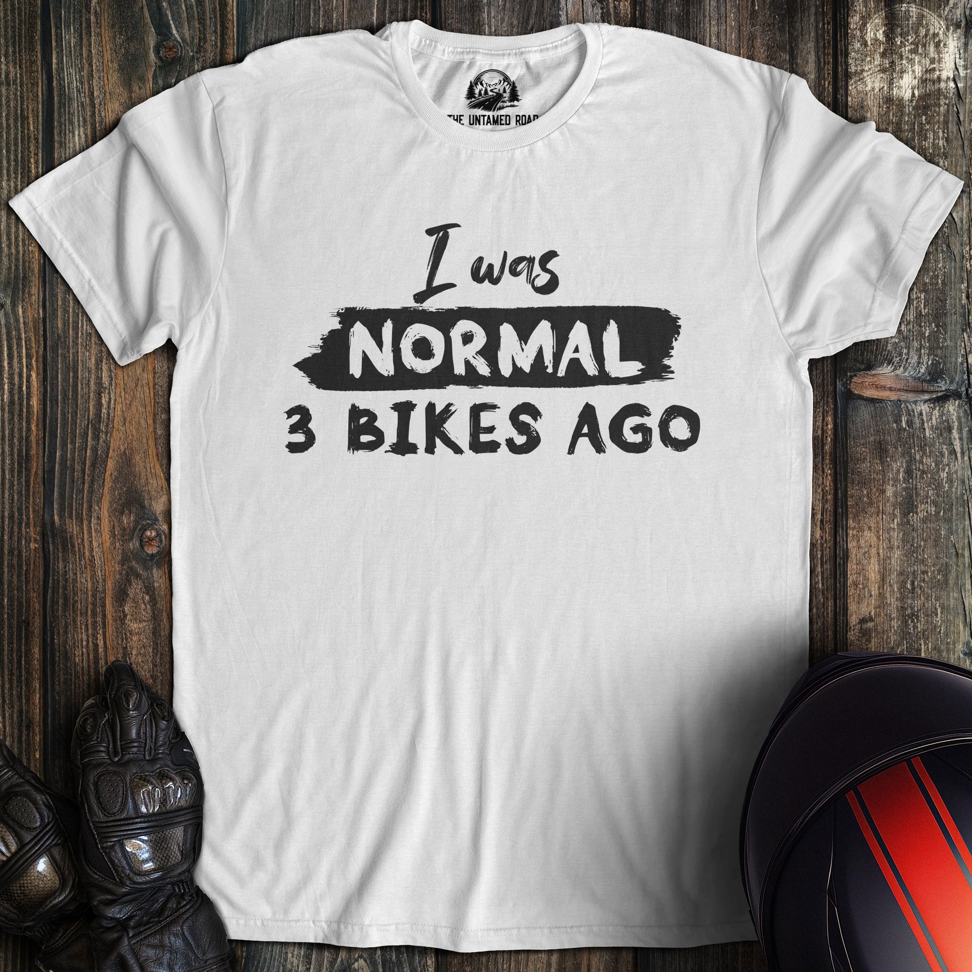 A white colored t-shirt with the words "normal three bikes ago" printed on the front.