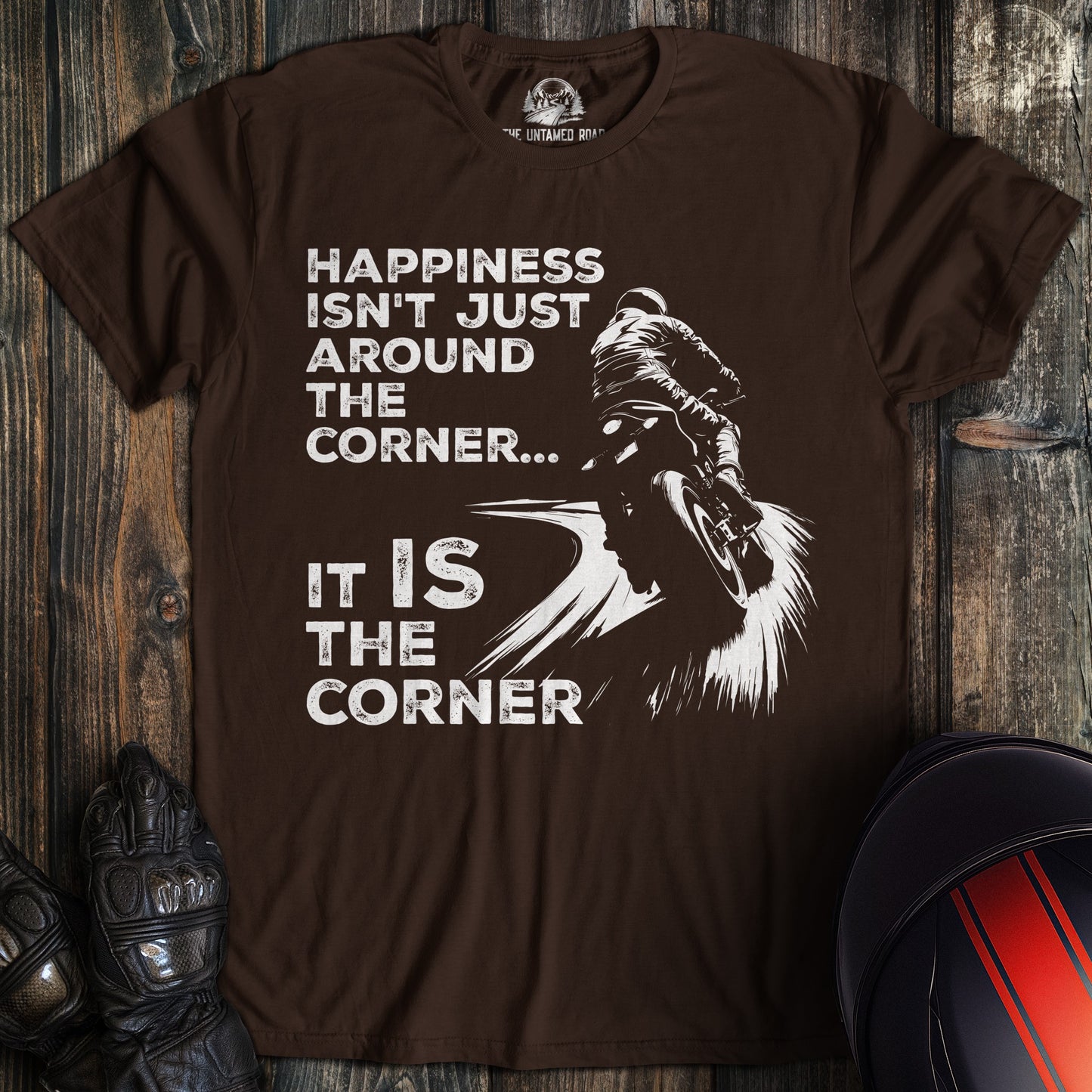 A dark chocolate colored t-shirt with the words "happiness is the corner" printed on the front.