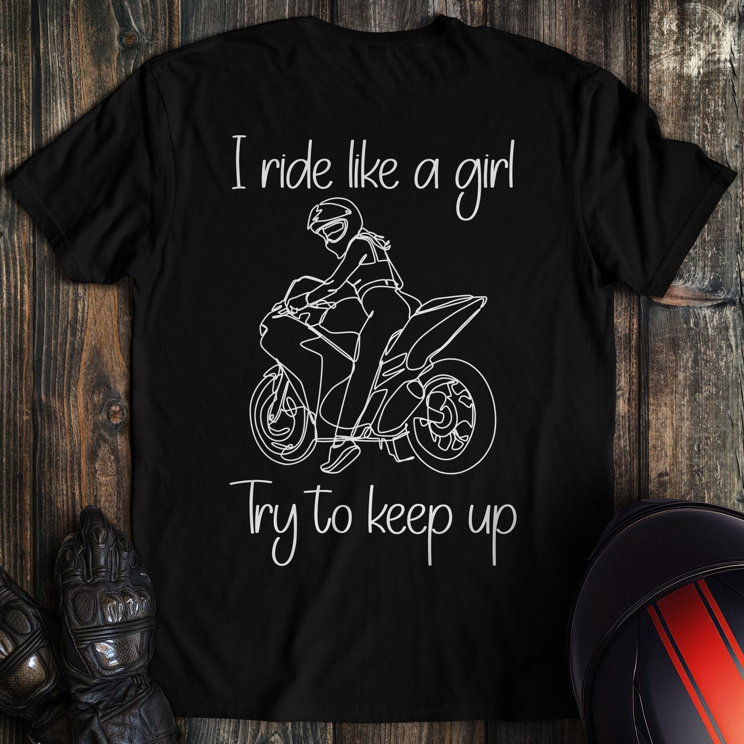 A black t-shirt featuring a white line drawing of a woman on a motorcycle with the text I ride like a girl Try to keep up.