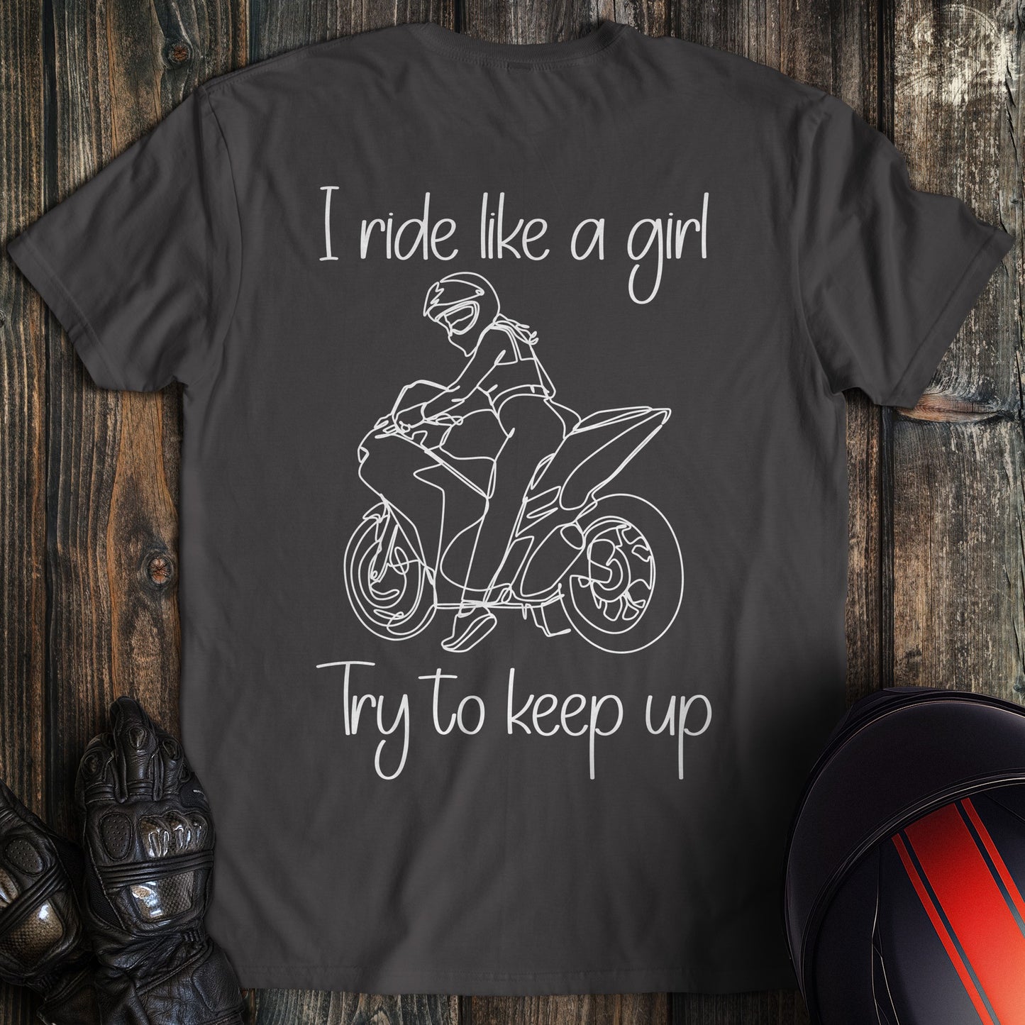 A charcoal gray t-shirt with a white line drawing of a woman on a motorcycle and the text, I ride like a girl Try to keep up.