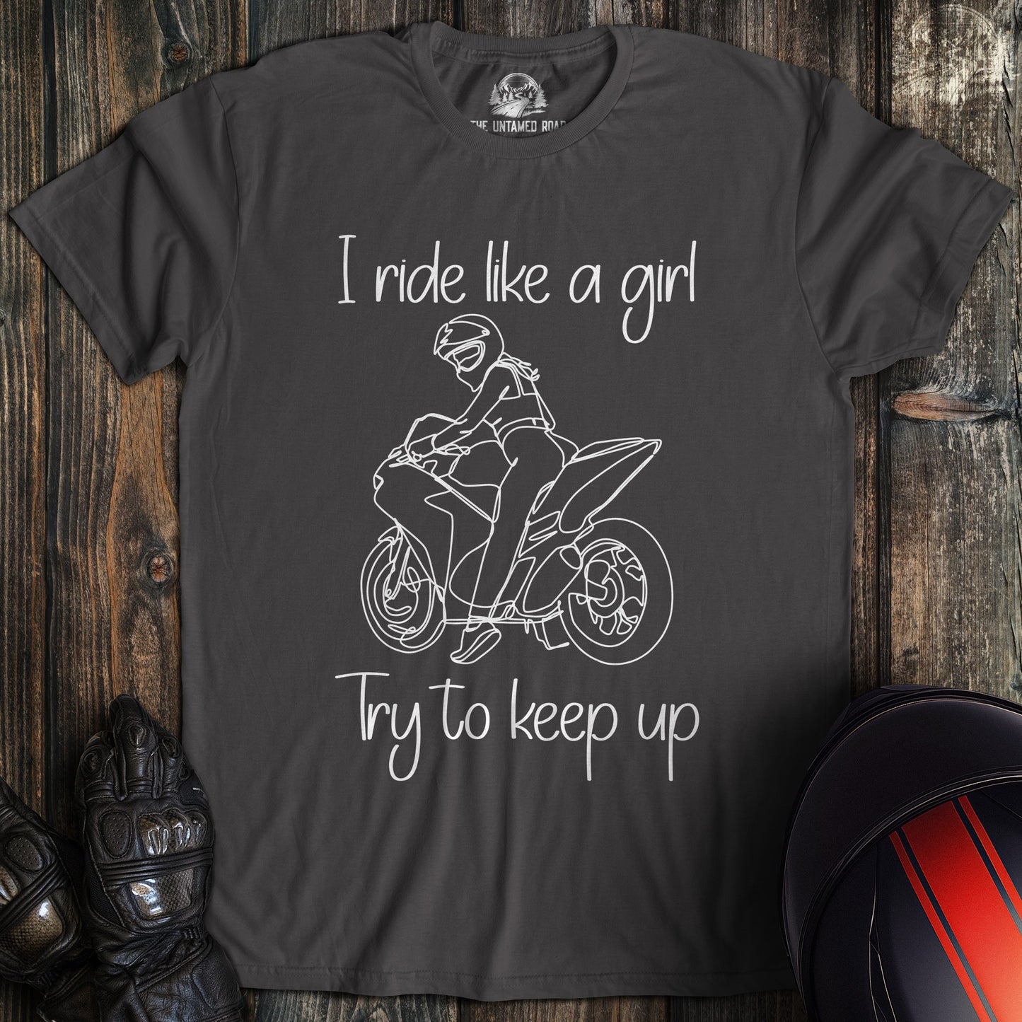 A charcoal gray t-shirt featuring a white line drawing of a woman on a motorcycle with the text I ride like a girl.