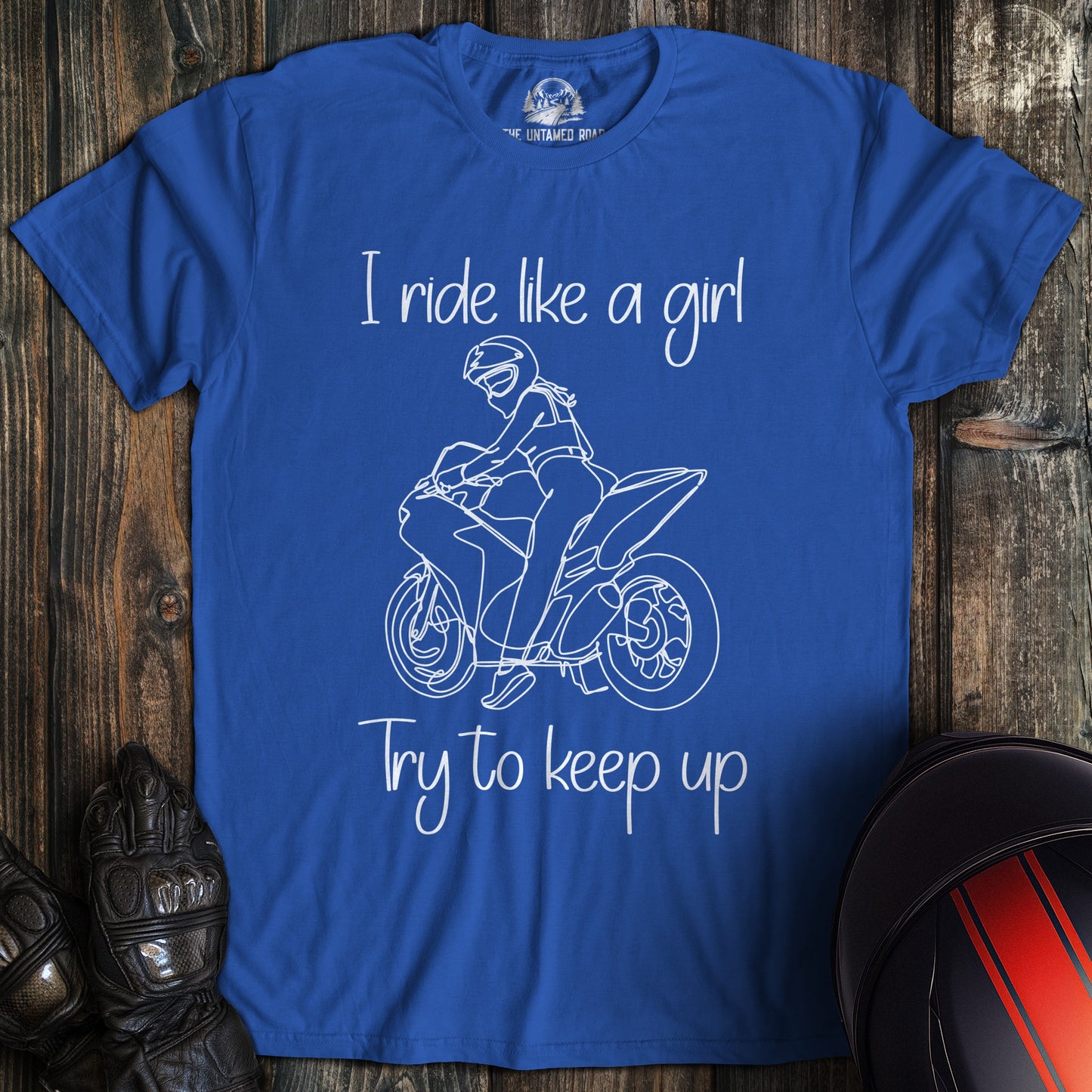 A royal blue t-shirt with a white line drawing of a woman on a motorcycle and the text I ride like a girl try to keep up.