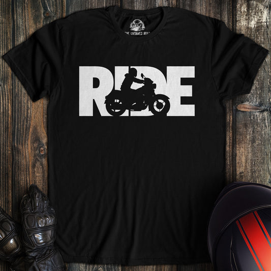 Black t-shirt with 'RIDE' graphic on a wooden surface with motorcycle helmet and glove.