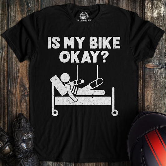 A black t-shirt featuring a funny biker graphic of a stick figure in a hospital bed with the text, IS MY BIKE OKAY?