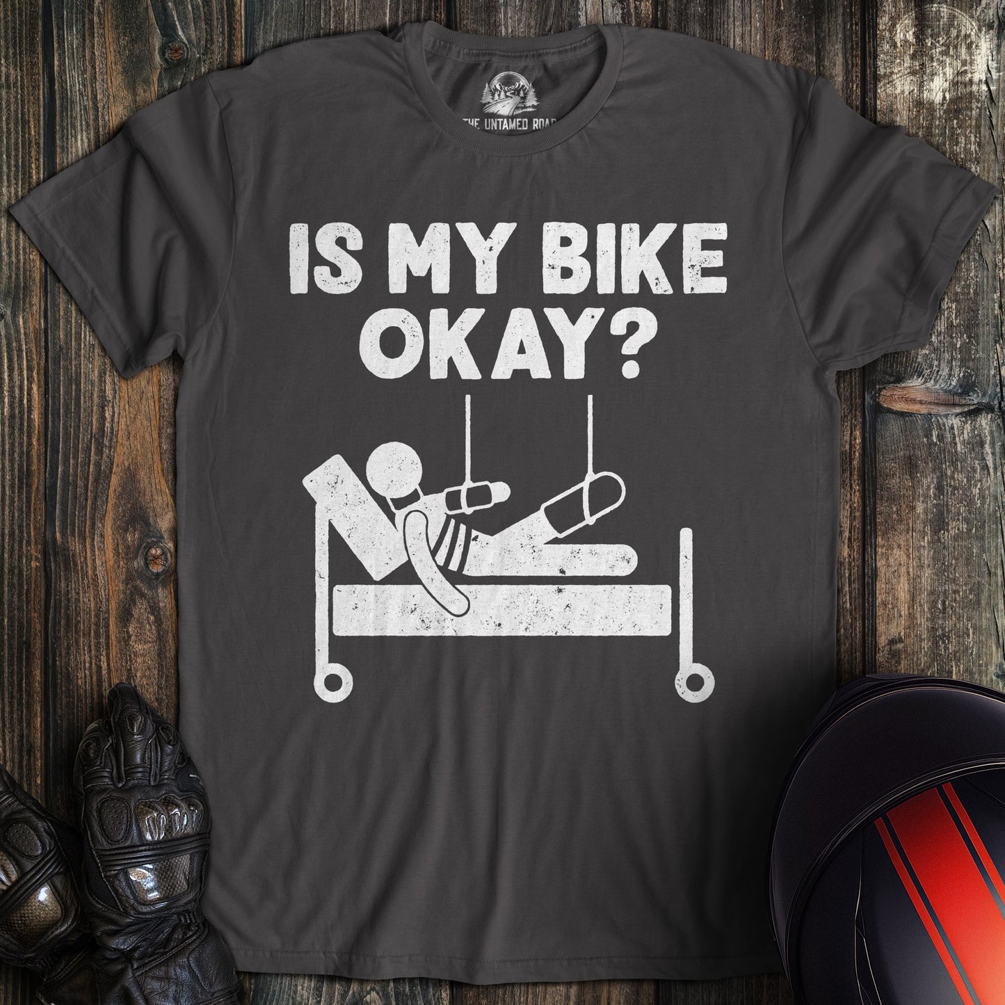 A charcoal gray t-shirt with a funny graphic of a person in a hospital bed and the text, Is My Bike Okay?