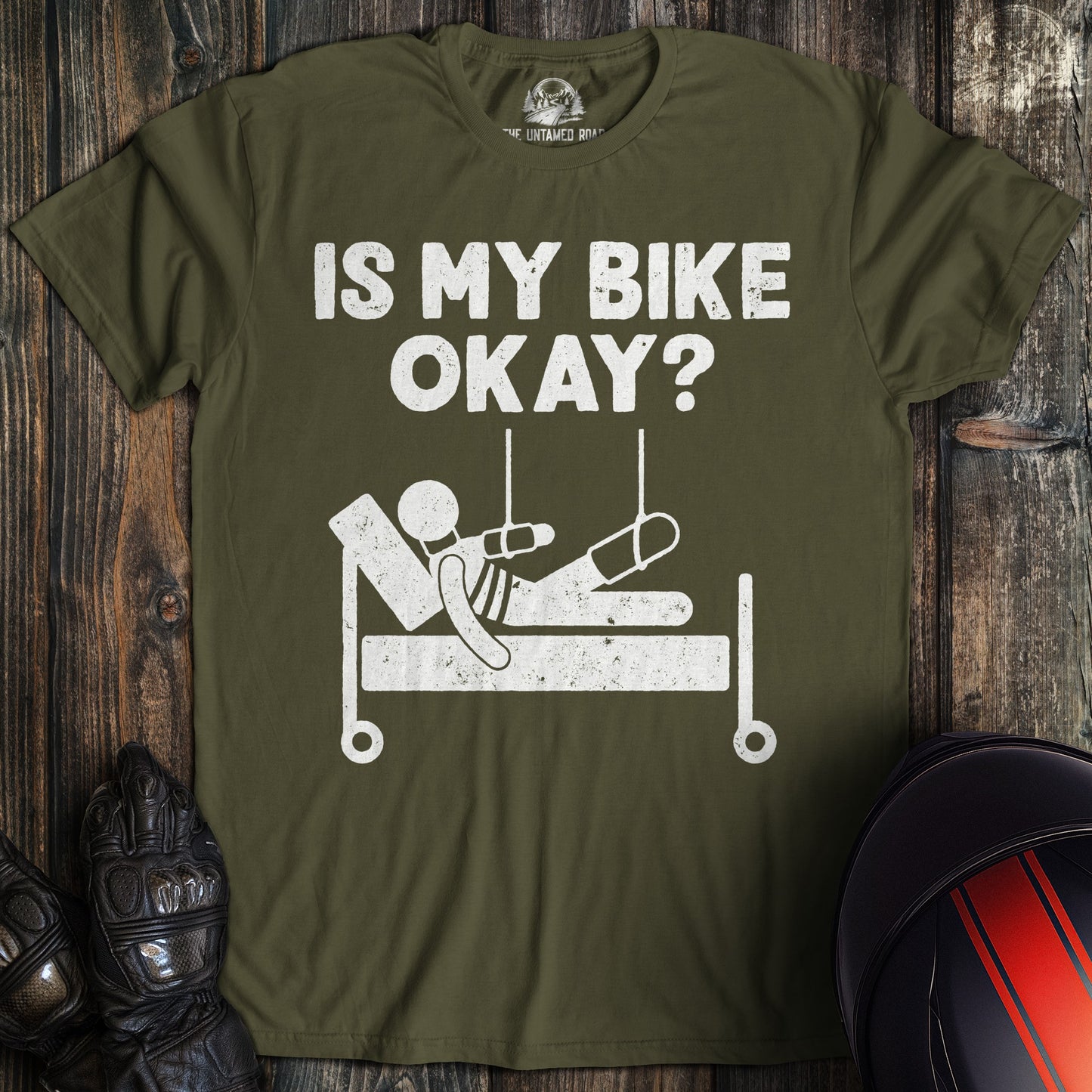 A military green t-shirt with a funny graphic of a person in a hospital bed and the text, Is My Bike Okay?