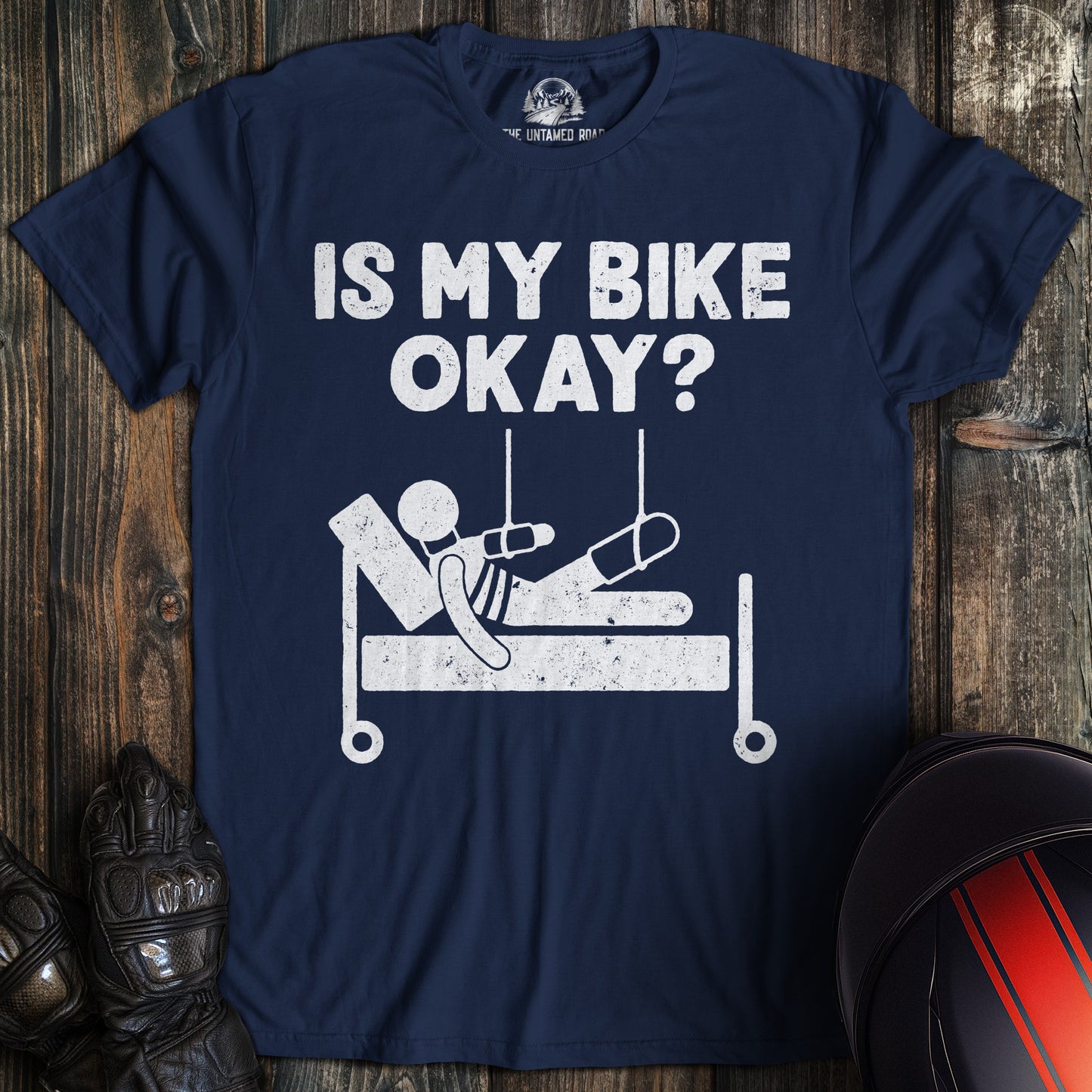 A navy blue t-shirt with a funny graphic of a person in a hospital bed and the text, Is My Bike Okay?
