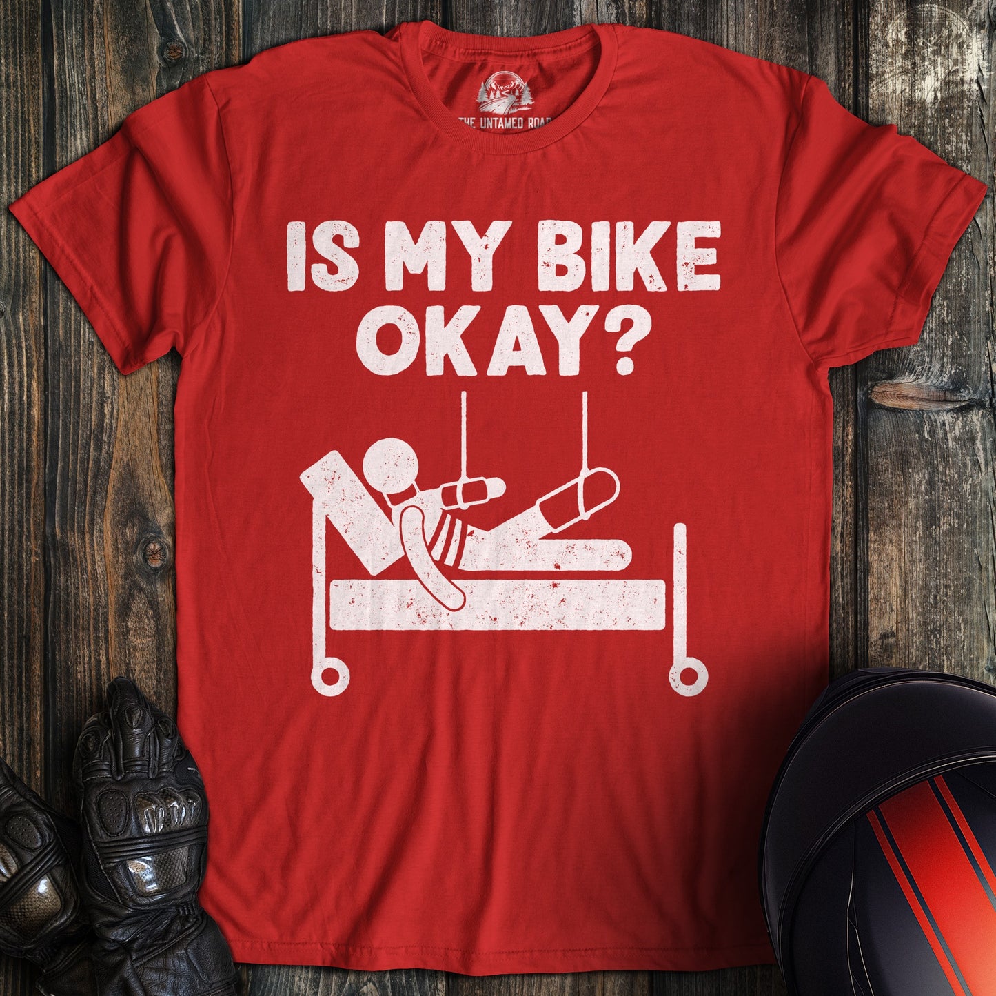 A red t-shirt with a funny graphic of a person in a hospital bed and the text, IS MY BIKE OKAY?
