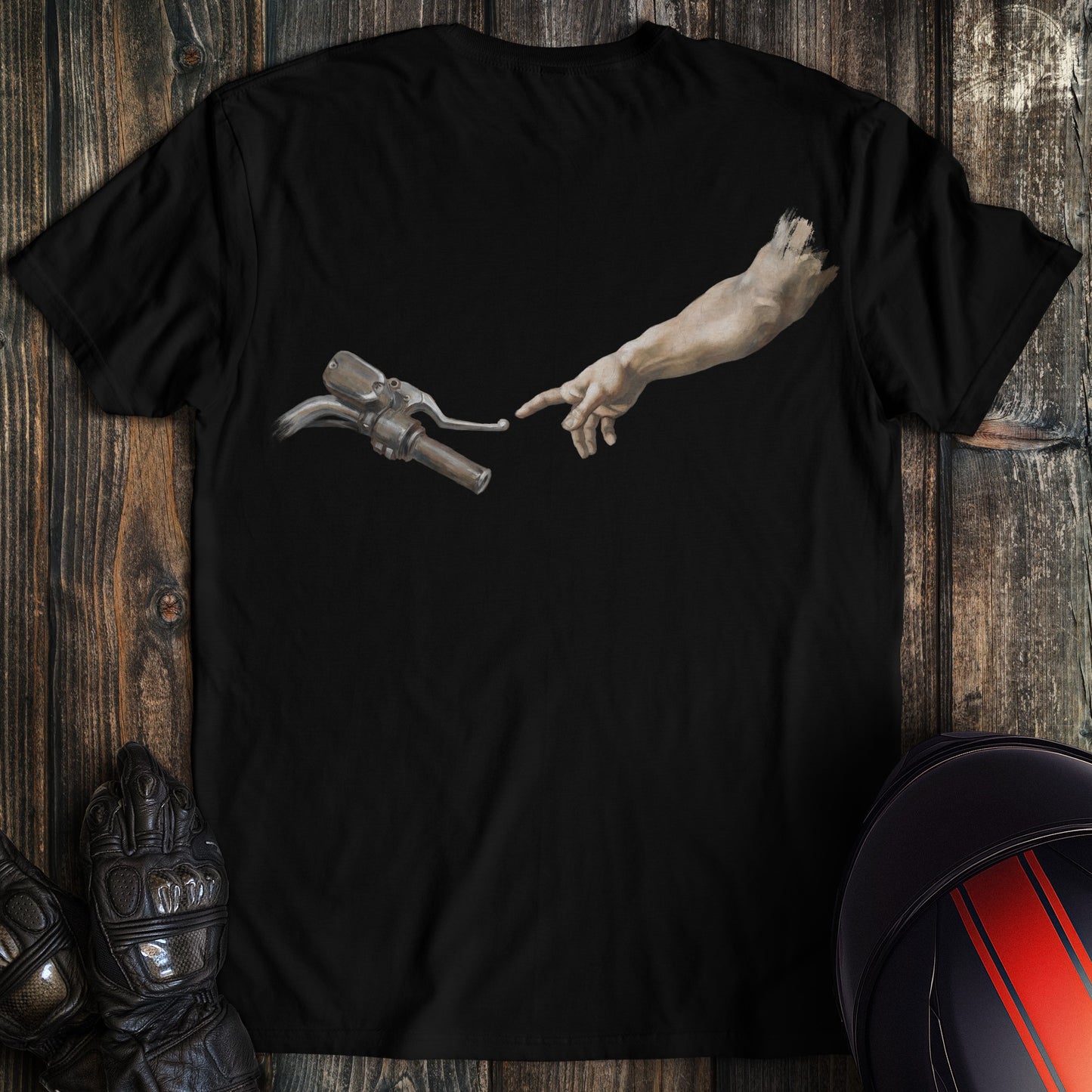 A black t-shirt featuring a funny graphic of a hand reaching toward a motorcycle handlebar in a parody of Adam's creation.