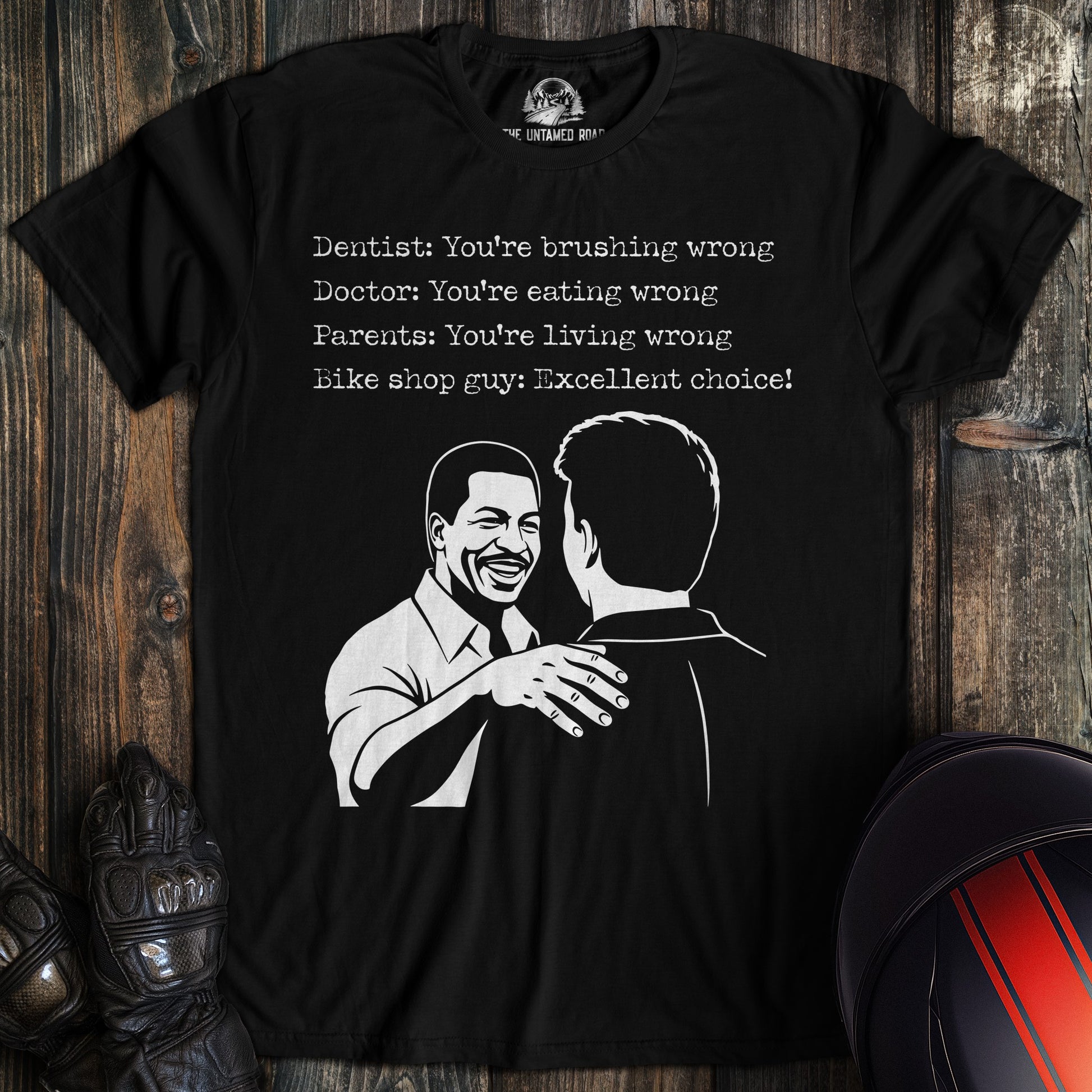 A black t-shirt featuring a funny biker graphic of two men and text ending with 'Bike shop guy: Excellent choice!'
