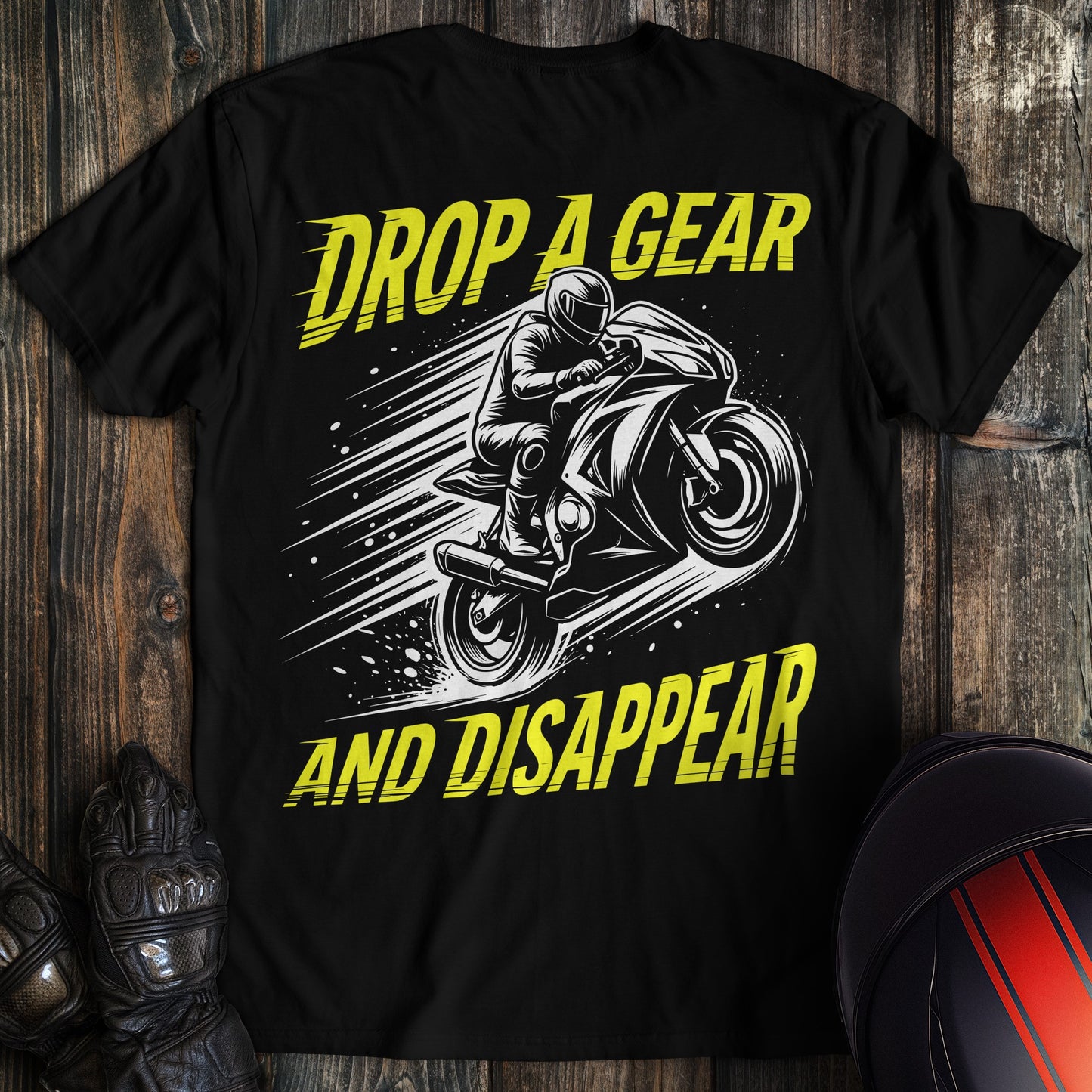 A black t-shirt with a yellow and white graphic of a biker on a motorcycle and the text Drop A Gear And Disappear.